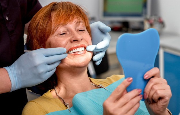 An older woman admiring her new denture with a hand mirror