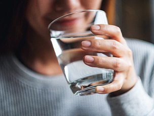 Woman in gray shirt drinking water from clear glass