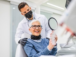 Woman with black glasses smiling at reflection in handheld mirror
