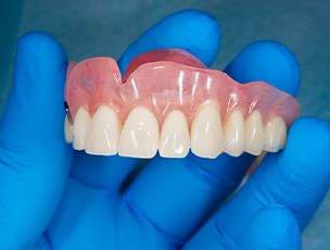 A gloved hand holding a removable denture