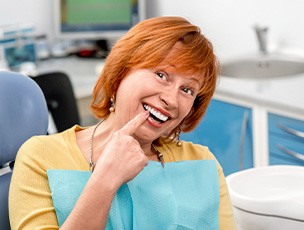 Red-headed woman in dental chair smiling pointing to her tooth