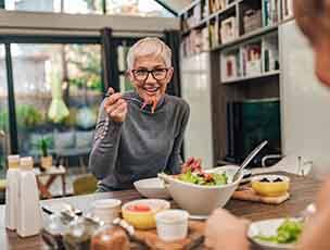 Woman smiling while eating lunch with friend in kitchen
