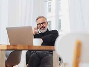Man smiling while talking on phone and working on laptop