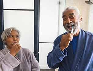 Couple smiling while brushing teeth in bathroom