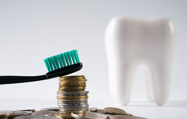Stack of coins and toothbrush in front of tooth in background