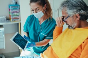 Dentist showing patient X-ray of teeth on a tablet.