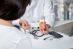 Dentist's hands holding model tooth discussing treatment with patient